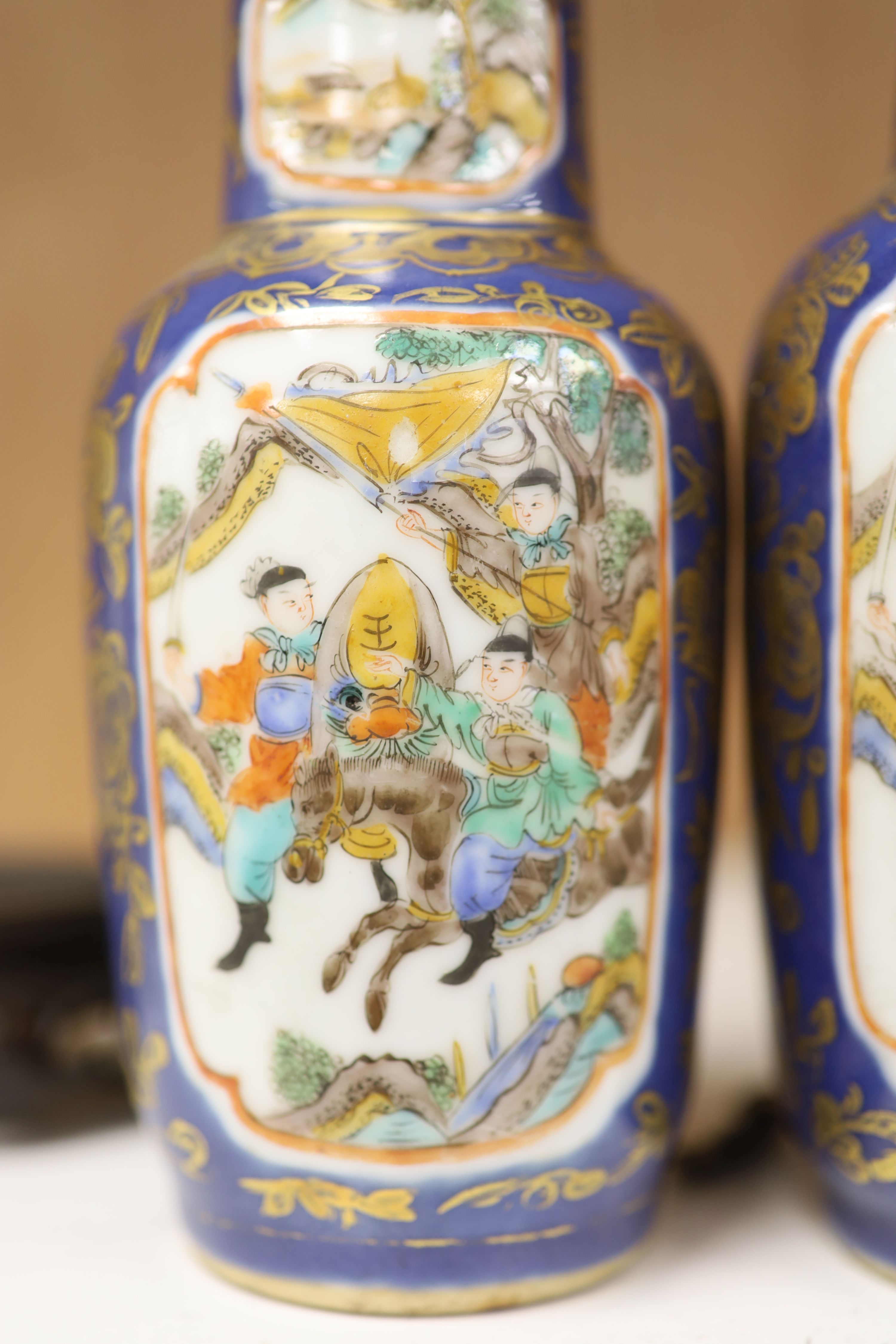 A pair of Chinese Kangxi style blue-ground vases, late 19th century decorated with panels of warriors and heightened in gilt, on carved hardwood stands, height 18cm excluding stand